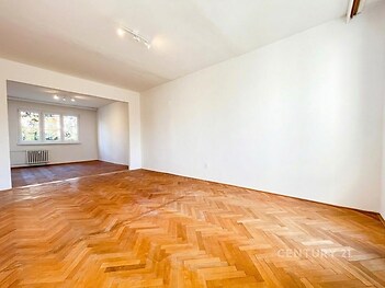 Světlý obývací pokoj s parketovou podlahou, velkými okny a bílými stěnami, moderní a prostorný, ideální pro rodinné bydlení