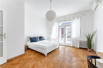 Prostorná ložnice s parketovou podlahou, velkými okny a moderní klimatizací, nabízí světlo a styl v rekonstruovaném bytě.