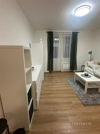 Světlý obývací pokoj s parketovou podlahou, moderním osvětlením a velkými okny, jednoduchý a útulný styl interiéru.