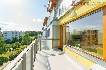 Prostorný balkon s moderním zábradlím, velká okna poskytující výhled na zeleň, světlá fasáda, ideální pro relaxaci.