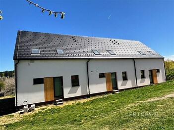 Moderní rodinný dům s moderní střechou, dřevěné obložení a velká okna, prostorný venkovní prostor na zeleném pozemku.