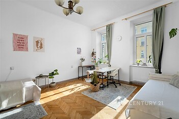 Světlý obývací pokoj s parketovou podlahou, velká okna poskytují dostatek přirozeného světla, moderní dekorace a výhled do ulice