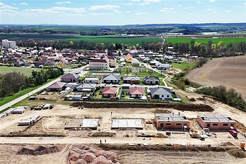 Nová výstavba rodinných domů vedle dokončeného obytného komplexu. Moderní design s červenými střechami a zahradami v klidné oblasti.