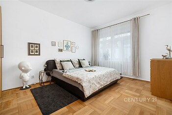 Prostorná ložnice s parketovou podlahou, velká okna zajišťují dostatek světla, moderní dekorace přispívá k příjemné atmosféře.