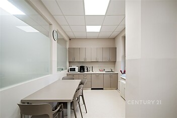 Moderní kuchyň s vestavěnými skříněmi a světlou dlažbou, nabízí prostorný jídelní kout a minimalistický design vhodný pro kancelářské prostředí.