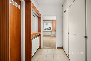 Vstupní chodba se světlou dlažbou a vestavěnými skříněmi, dřevěné obložení, vede do světlého obývacího pokoje, moderní styl.