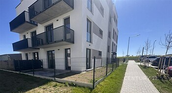 Moderní bytový dům s balkony, bílou fasádou a udržovaným trávníkem, v klidné lokalitě.