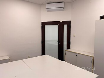 Pracovní kancelář s bílými stěnami, klimatizací a vestavěnou skříní v rohu.