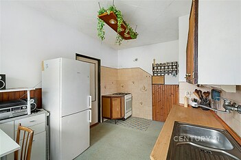 Kuchyň s retro dlažbou, dřevěným obložením a plynovým sporákem, vybavená lednicí a vestavěnými skříněmi, nabízí útulné bydlení.