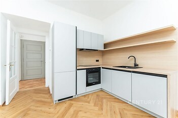 Moderní kuchyň s parketovou podlahou, vestavěnými spotřebiči a světlými dřevěnými povrchy, nabízí elegantní a praktický design.