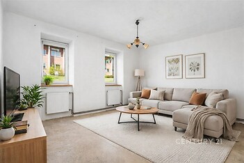 Světlý obývací pokoj s moderními betonovými podlahami, velkými okny a světlým nábytkem, vytvářejícími příjemnou atmosféru.