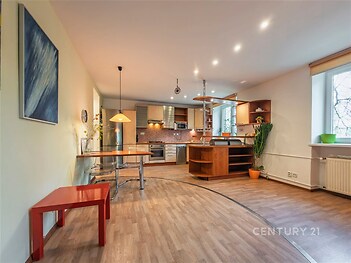 Moderní kuchyň s parketovou podlahou, vestavěnými spotřebiči a velkým oknem umožňujícím dostatek přirozeného světla.