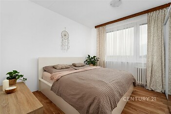 Světlá ložnice s parketovou podlahou, velkými okny a závěsy, moderní zařízení, dřevěný nábytek, útulný interiér.