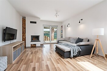 Světlý obývací pokoj s parketovou podlahou, moderní krbová kamna a velká okna, které zajišťují dostatek přirozeného světla