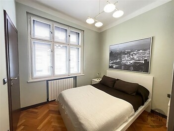 Světlá ložnice s parketovou podlahou a velkými okny, moderní nástěnné osvětlení, konfortní atmosféra, světlý a stylový design.