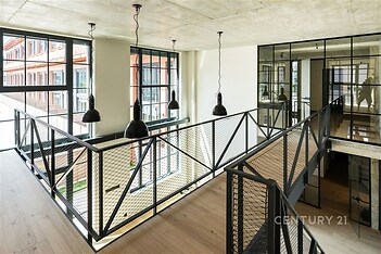 Světlá moderní chodba s velkými okny, průmyslovým stylem a dřevěnou podlahou. Skleněné stěny oddělují prostory a dodávají industriální vzhled.