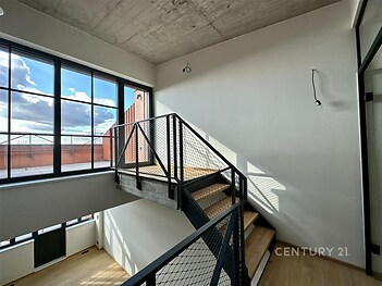 Schodiště s moderním designem, dřevěné stupně a kovové zábradlí, velká okna zajišťující světlé a prostorné prostředí, industriální styl.