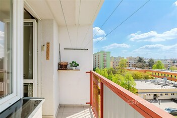 Balkón s keramickou dlažbou, červeným zábradlím a výhledem na městskou panoramu. Světlý a prostorný venkovní prostor.