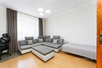 Světlý obývací pokoj s parketovou podlahou, moderní šedá sedací souprava, velká okna s bílými závěsy, minimalistický styl interiéru.