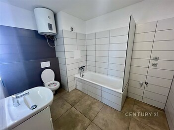 Koupelna s moderními dlaždicemi, vanou a světlým obkladem. Kombinace tmavých a světlých tónů vytváří elegantní atmosféru.