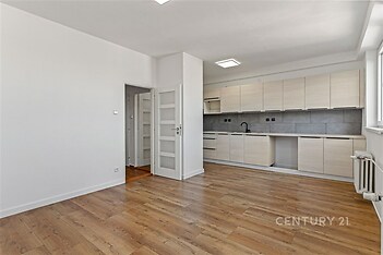 Světlý obývací pokoj s moderní kuchyní, parketová podlaha, vestavěné skříně a velká okna poskytují dostatek přirozeného světla