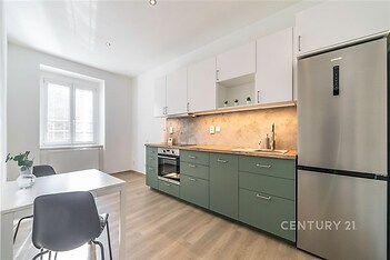 Moderní kuchyň se zelenými skříňkami, světlou parketovou podlahou a vestavěnými spotřebiči, světlý prostor díky velkému oknu.