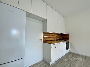 Moderní kuchyň s dřevěnou pracovní deskou, vestavěnými spotřebiči a světlou laminátovou podlahou, nabízí elegantní úložná řešení.