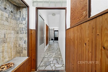 Úzká vstupní chodba s dřevěným obložením a kamennou dlažbou, moderní design, světlé stěny, skleněné dveře vedoucí do další místnosti.