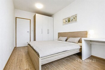 Prostorná ložnice s parketovou podlahou, vestavěné skříně a moderní nábytek, světlý interiér s minimalistickým designem.