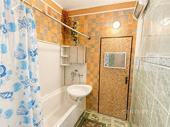 Koupelna se světlými dlaždicemi, vestavěnými úložnými skříněmi a sprchovým koutem. Retro styl a praktické uspořádání prostoru.