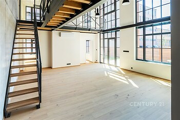 Světlý obývací pokoj s parketovou podlahou, velká okna a moderní průmyslový styl.