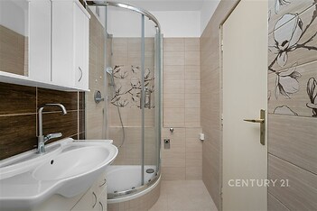 Moderní koupelna s dlažbou, sprchový kout s posuvnými dveřmi, světlé obklady a elegantní umyvadlo, čistý a udržovaný prostor.