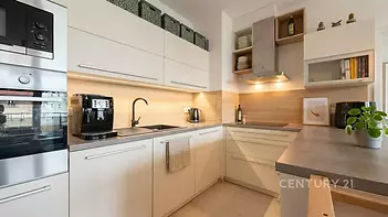 Moderní kuchyň s vestavěnými spotřebiči, světlou dřevěnou linkou a parketovou podlahou, ideální pro stylové bydlení.