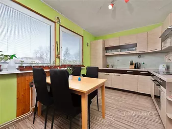 Kuchyň s moderními dřevěnými skříňkami, světlou parketovou podlahou a velkými okny, která poskytují dostatek přirozeného světla.