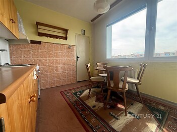 Kuchyň s dlažbou a dřevěným nábytkem, velké okno poskytuje dostatek světla, rustikální styl vytváří útulnou atmosféru v bytě.