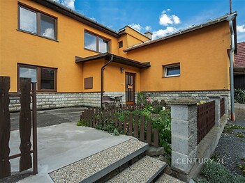 Vstupní prostor rodinného domu s pískovcovou fasádou a dřevěným plotem, nachází se na klidné ulici.