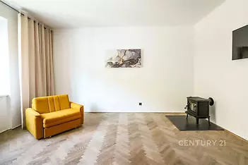Světlý obývací pokoj s parketovou podlahou, krbová kamna dodávají útulnost, moderní minimalistický design a velké okno pro přirozené světlo