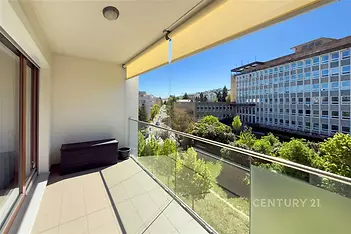 Prostorná lodžie s dlažbou, skleněným zábradlím a výhledem na městskou krajinu, ideální pro moderní byt.