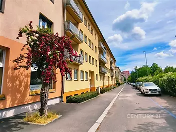 Řadový bytový dům s barevnou fasádou, balkony a stromy v klidné ulici, moderní prostředí, v blízkosti zeleně a dopravní dostupnosti