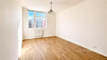 Světlý pokoj s dřevěnou podlahou, velkými okny a moderní výmalbou.
