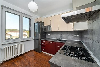 Moderní kuchyň s dřevěnou podlahou nabízí vestavěné spotřebiče, tmavou pracovní desku a velká okna pro dostatek světla.