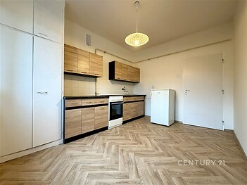 Moderní kuchyň s parketovou podlahou, dřevěnými skříňkami a vestavěnými spotřebiči vytváří světlý a elegantní prostor vhodný pro rodinné vaření.