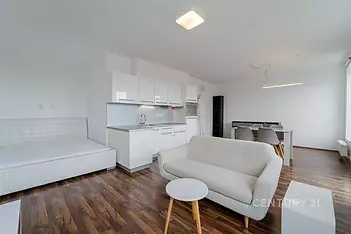 Moderní obývací pokoj s kuchyňským koutem, parketová podlaha, světlý interiér, velká okna, minimalistický styl.