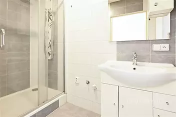 Moderní koupelna s betonovou dlažbou, sprchovým koutem a bílým umyvadlem. Kombinace šedých a bílých obkladů vytváří čistý vzhled.