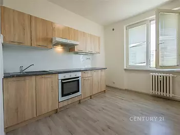 Moderní kuchyň s dřevěnými skříňkami, světlé parketové podlahy a velká okna zajišťující dostatek přirozeného světla.