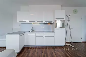 Moderní kuchyň s bílými lesklými skříňkami, vestavěnou troubou a parketovou podlahou, prostorný design pro pohodlné bydlení.