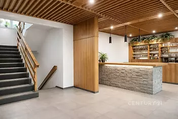 Recepční prostor s moderním designem, dřevěným obložením a kamenným pultem, doplněný kovovými svítidly a parketovou podlahou pro stylový vzhled.