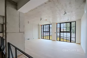 Světlý obývací pokoj s velkými okny, betonovým stropem a dřevěnou podlahou nabízí moderní a industriální atmosféru.
