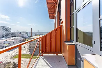 Moderní balkón s ocelovým zábradlím, nabízí výhled na městskou krajinu. Světlý prostor s moderním designem a slunečním světlem.