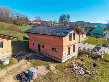 Nedokončený rodinný dům s červeným cihlovým zdivem a tmavou střechou na klidném místě s výhledem na přírodu, moderní architektura.